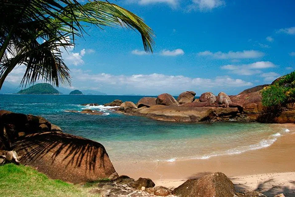 Enseada de águas turquesa em Ubatuba com costão de pedras e coqueiros no Centro