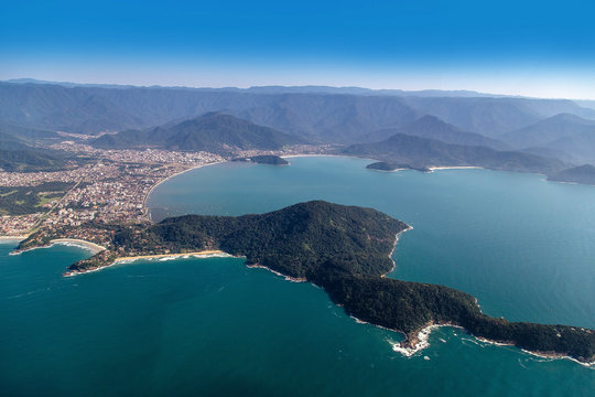 Vista aérea da enseada de Ubatuba, com a orla urbana à esquerda e a mata da ponta preservada à direita
