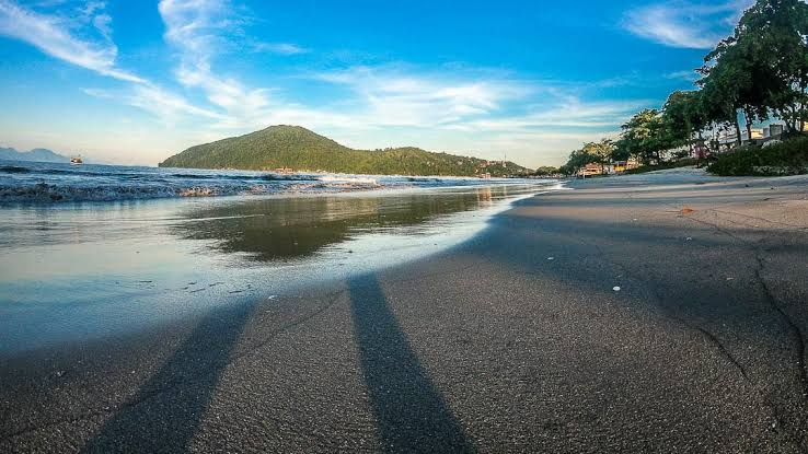 Faixa de areia da Praia de Itaguá em Ubatuba, com mar calmo e a Serra do Mar ao fundo