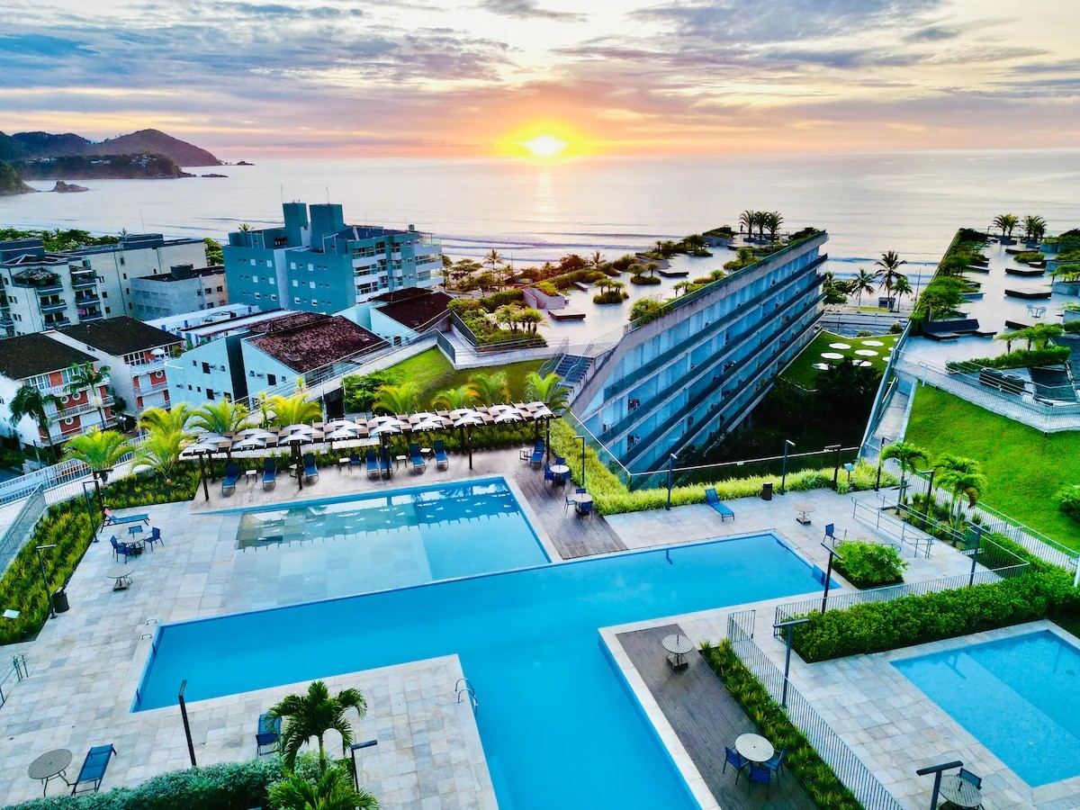 Rooftop do condomínio DNA na Praia Grande, Ubatuba, com piscinas de frente para o mar ao pôr do sol