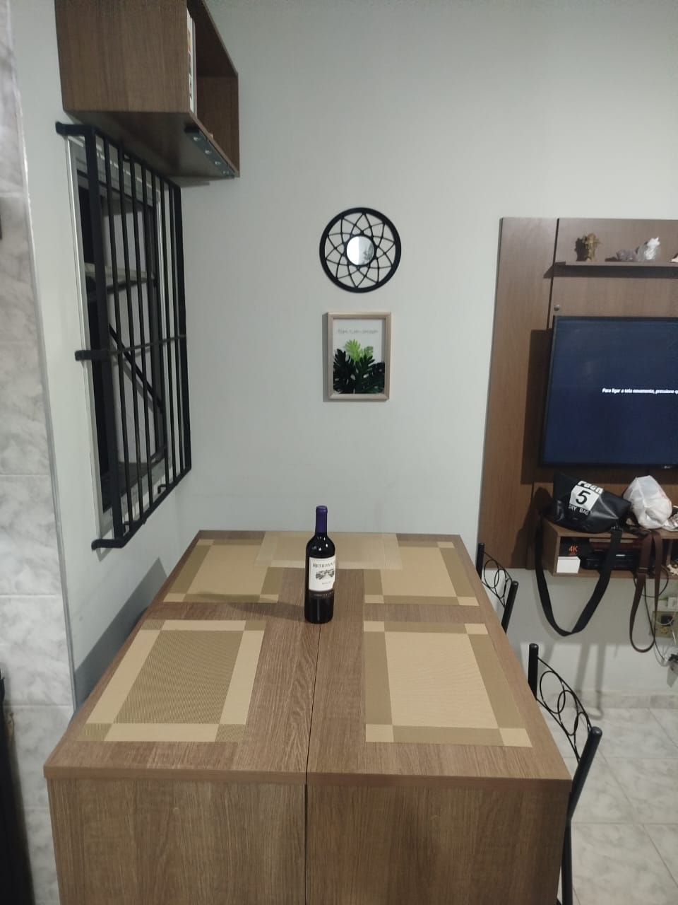 Ambiente de jantar com painel de TV e rack no apartamento mobiliado em Itaguá
