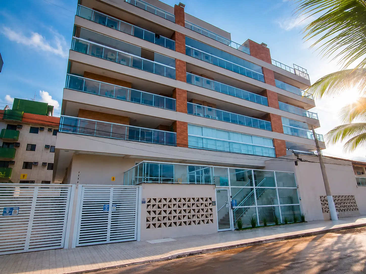 Fachada do Residencial Alpha Prime na Praia do Tenório, Ubatuba, com sacadas envidraçadas e portões brancos